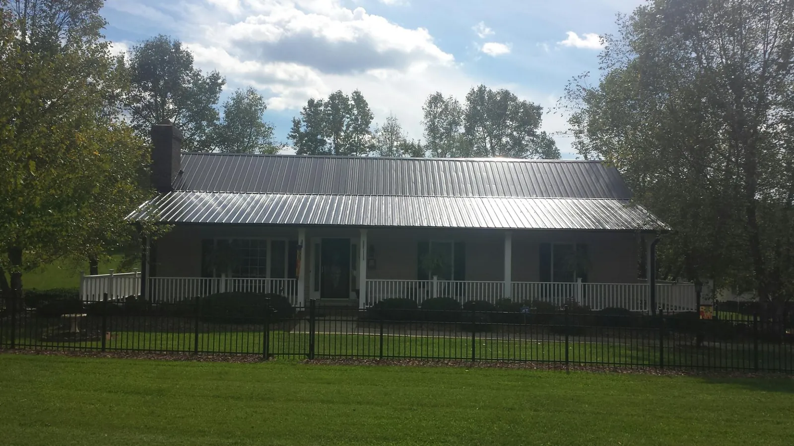 Gray metal roof on a brick ranch with a full width front porch — Gutter Guard Installation work by our crew in Caledonia
