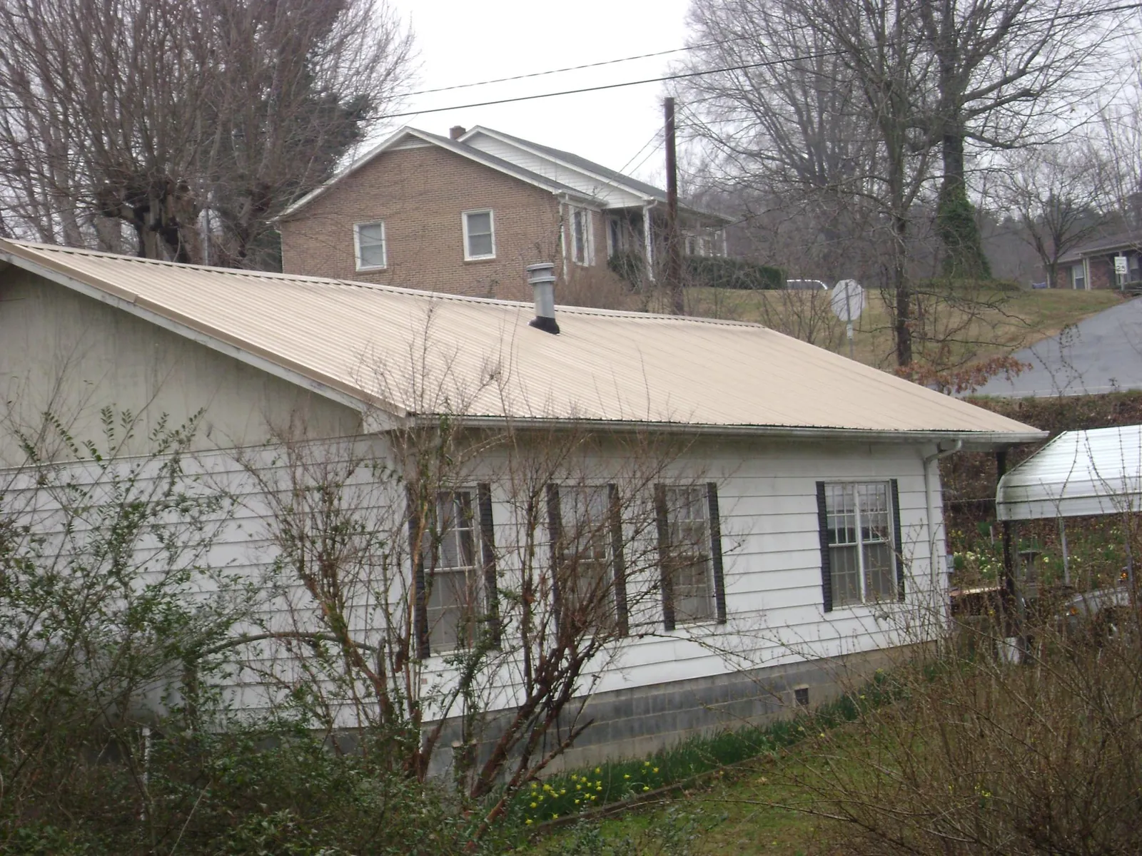 Tan metal roof on a white sided house set into a hillside — Commercial Roofing by Roofing Brothers in Caledonia